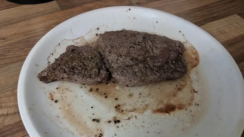 A disgusting-looking, gray microwaved steak on a plate.